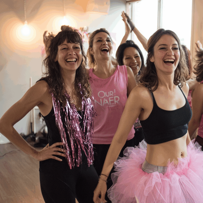 Moment de joie et de complicité lors d'un atelier privé Folk & Curious : un groupe d'amies en tenue décontractée prend la pose en riant pendant un cours de danse pour un enterrement de vie de jeune fille.
