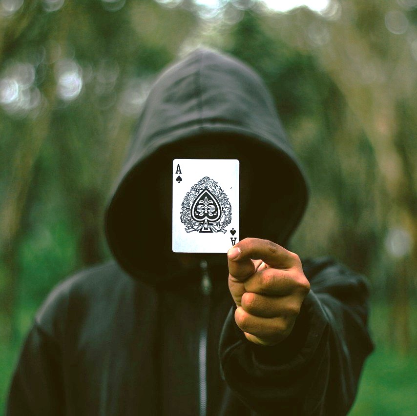 Folk&Curious : Team building de magie. Magicien cachant son visage avec une carte à jouer (as de pique)