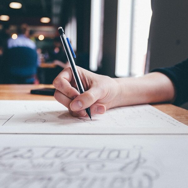 Folk&Curious : team building d'écriture intéractive. Main d'un participant dessinant des lettres au crayon sur du papier.