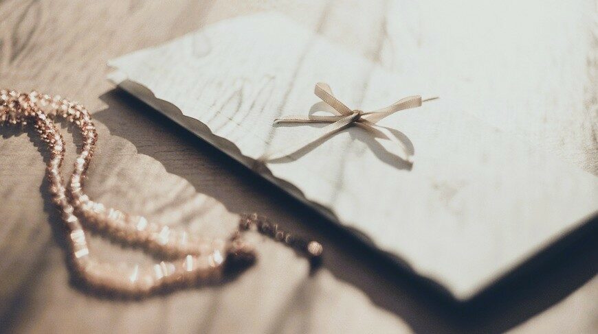 Folk&Curious : papeterie de mariage sur-mesure. Faire-part délicat avec un ruban fin, posé à côté d'un bijou de mariée.