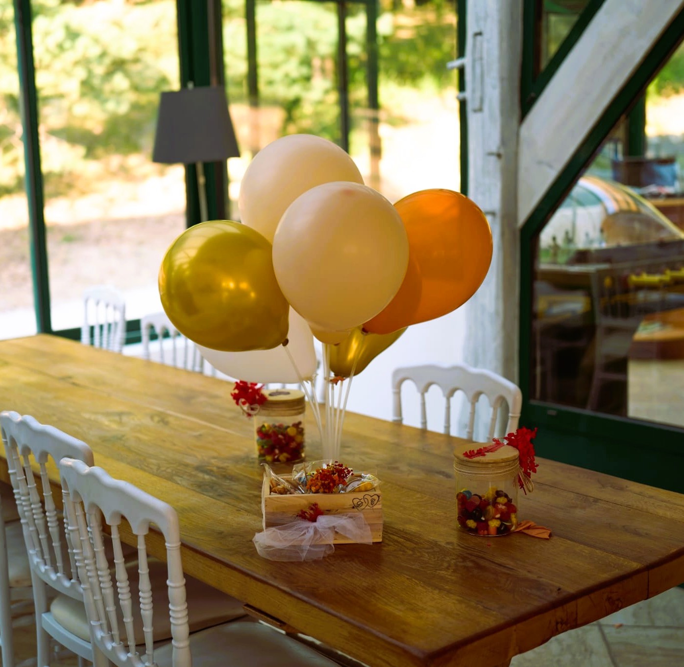 Table de mariage décorée avec simplicité : ballons dorés et bocaux gourmands dans la lumière d'une verrière
